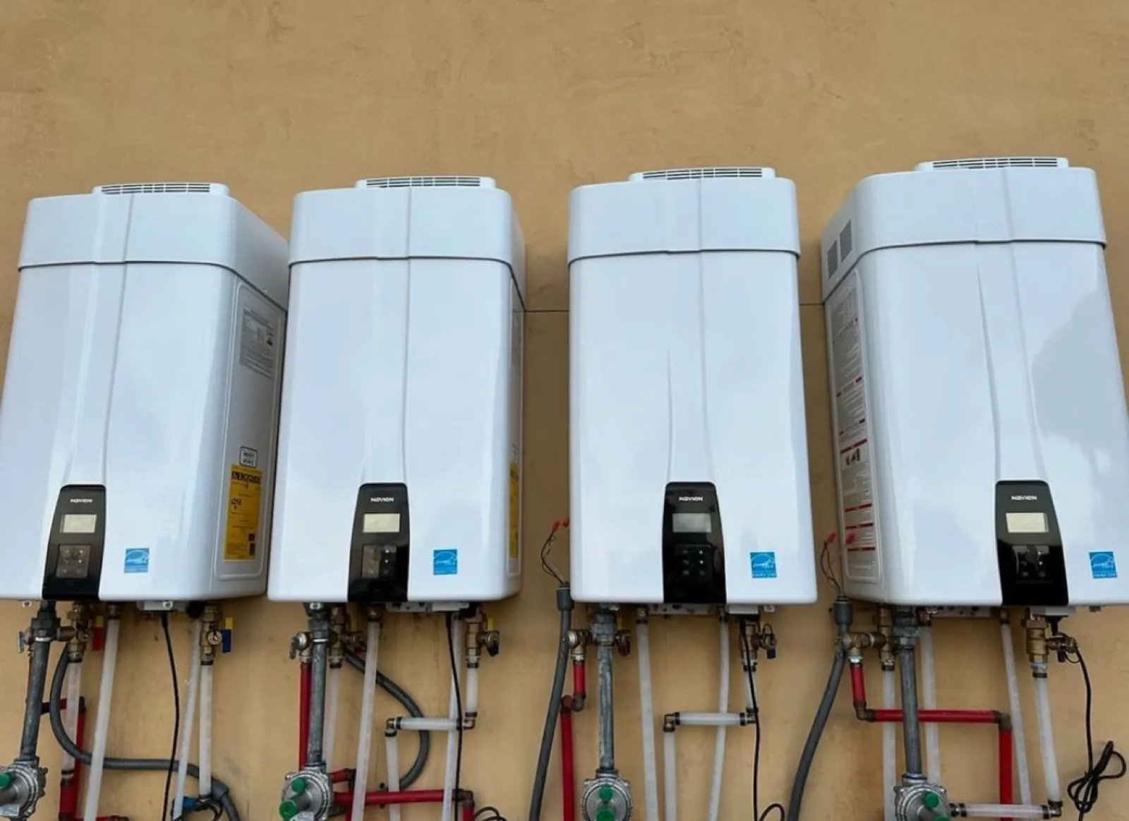 Four Navien tankless water heaters mounted side by side on an exterior wall