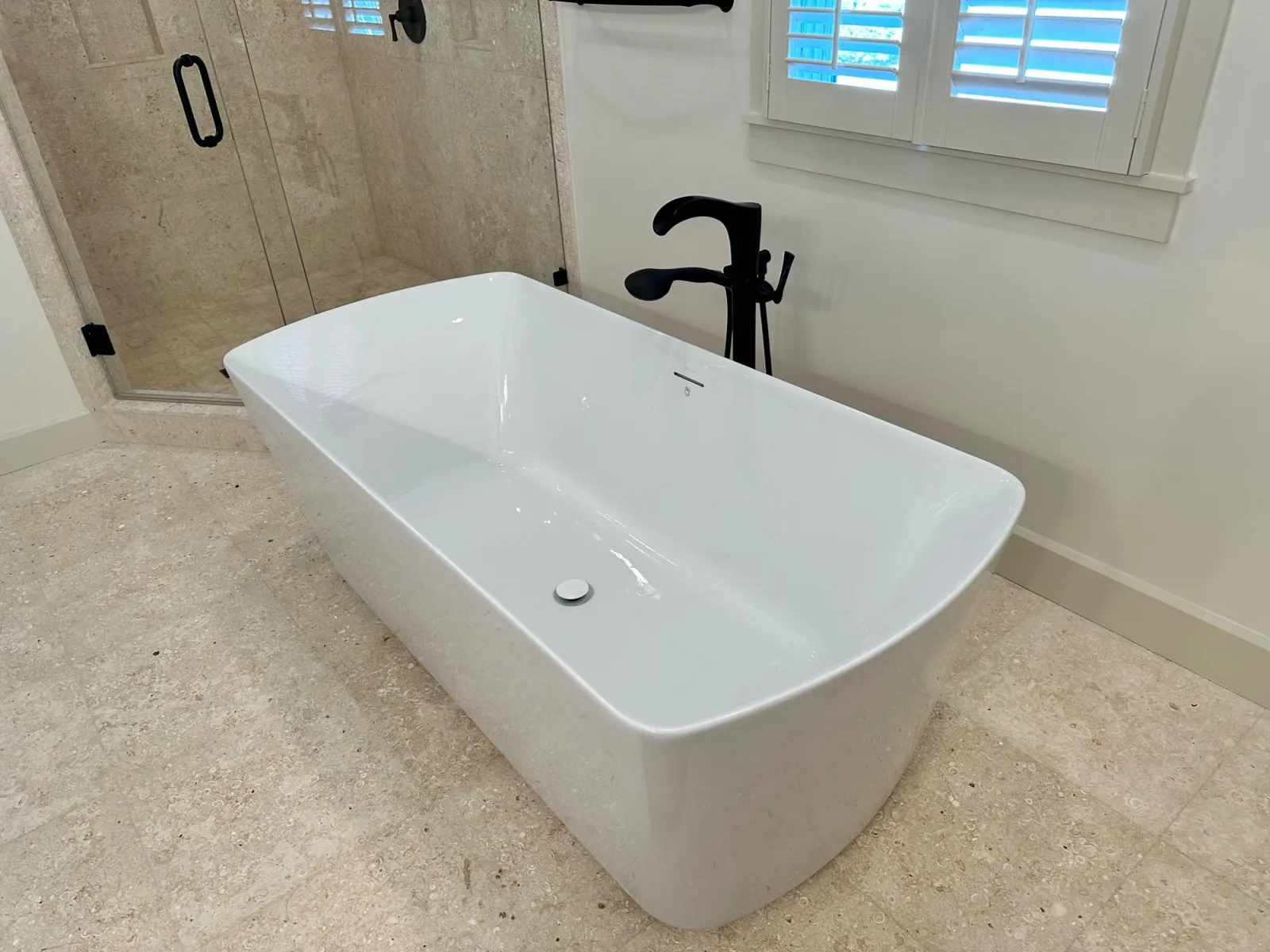 Freestanding bathtub with black fixtures beside a tiled shower